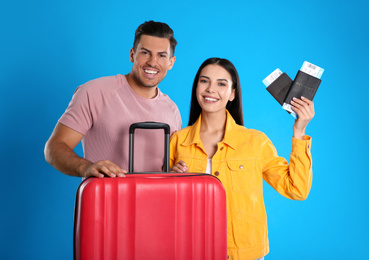 Photo of Happy couple with suitcase and tickets in passports for summer trip on blue background. Vacation travel