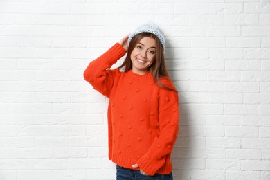 Beautiful young woman in warm sweater with hat near white brick wall