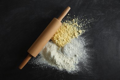 Photo of Rolling pin and different types of flour on black table, top view