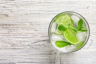 Photo of Refreshing beverage with mint and lime in glass on wooden background, top view