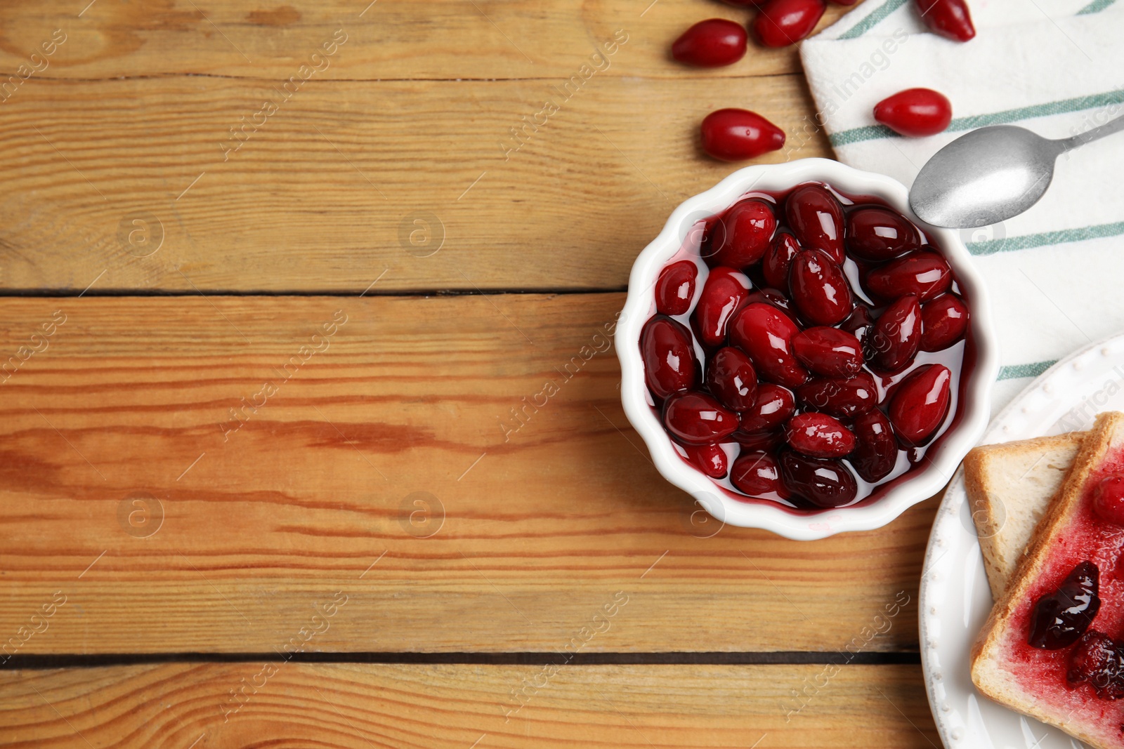 Photo of Delicious dogwood jam with berries and bread on wooden table, flat lay. Space for text