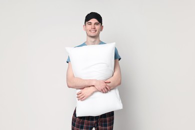 Happy man in pyjama and sleep mask holding pillow on light grey background