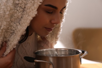 Photo of Woman with plaid doing inhalation above saucepot indoors