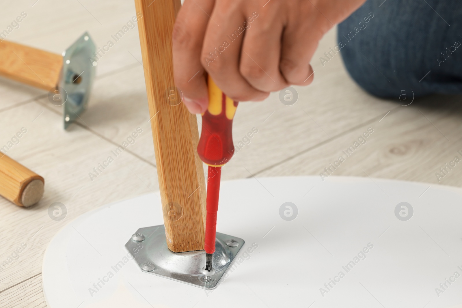 Photo of Man with screwdriver assembling furniture on floor, closeup