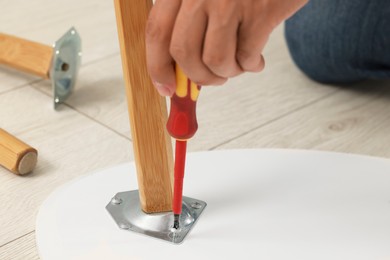 Photo of Man with screwdriver assembling furniture on floor, closeup