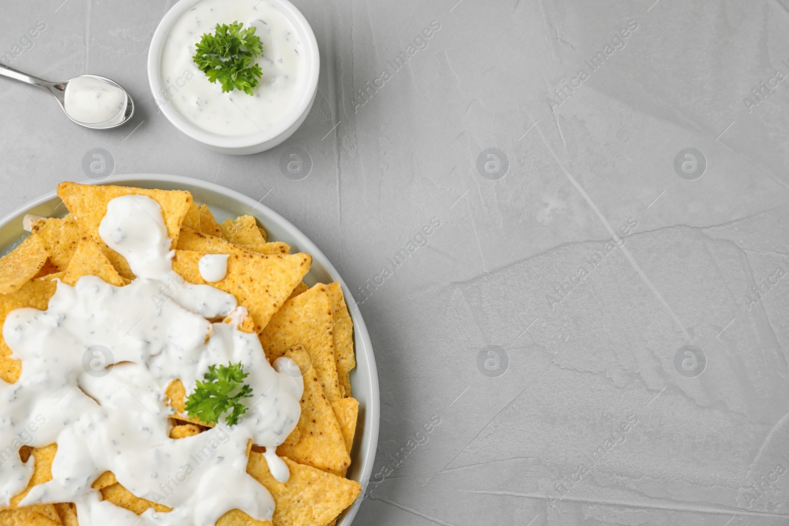 Photo of Plate of Mexican nacho chips with sauce on grey table, flat lay. Space for text