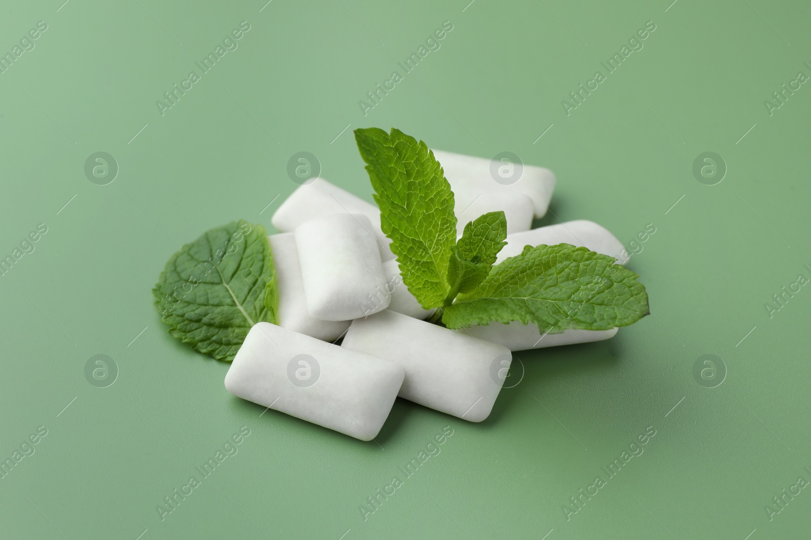 Photo of Tasty white chewing gums and mint leaves on light green background, closeup