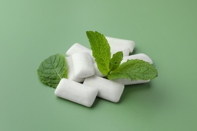 Tasty white chewing gums and mint leaves on light green background, closeup