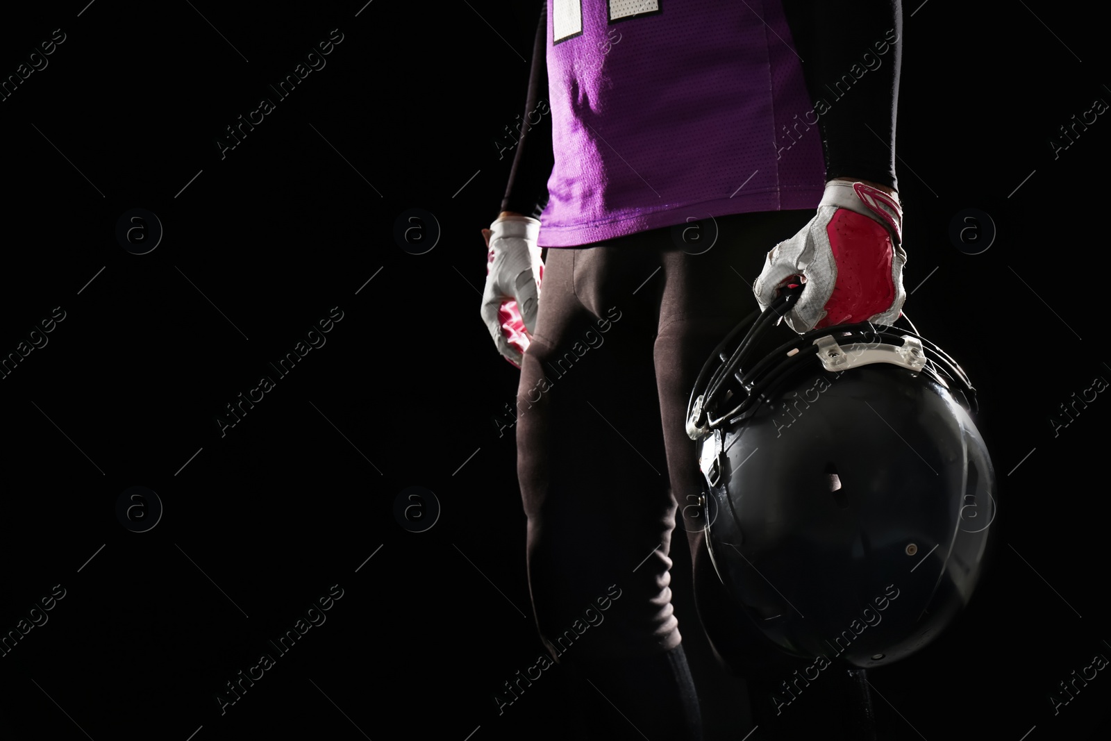 Photo of American football player with helmet wearing uniform on dark background, closeup. Space for text