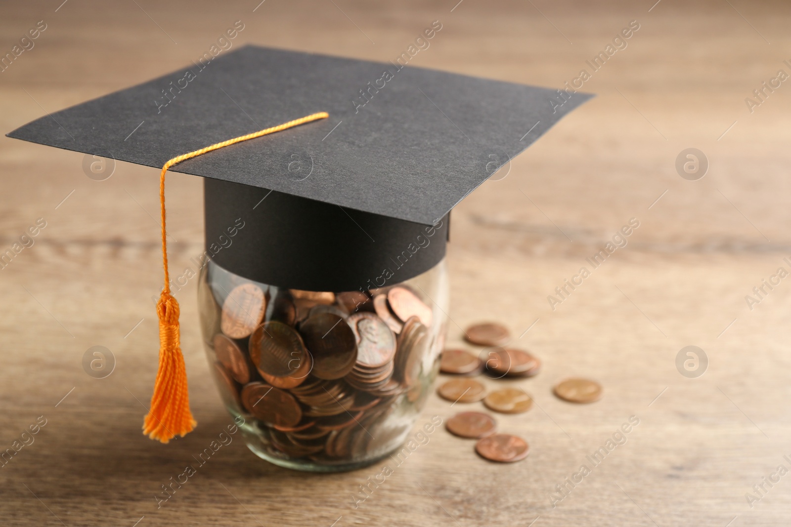Photo of Graduation hat and jar with coins on wooden table, space for text. Money saving concept
