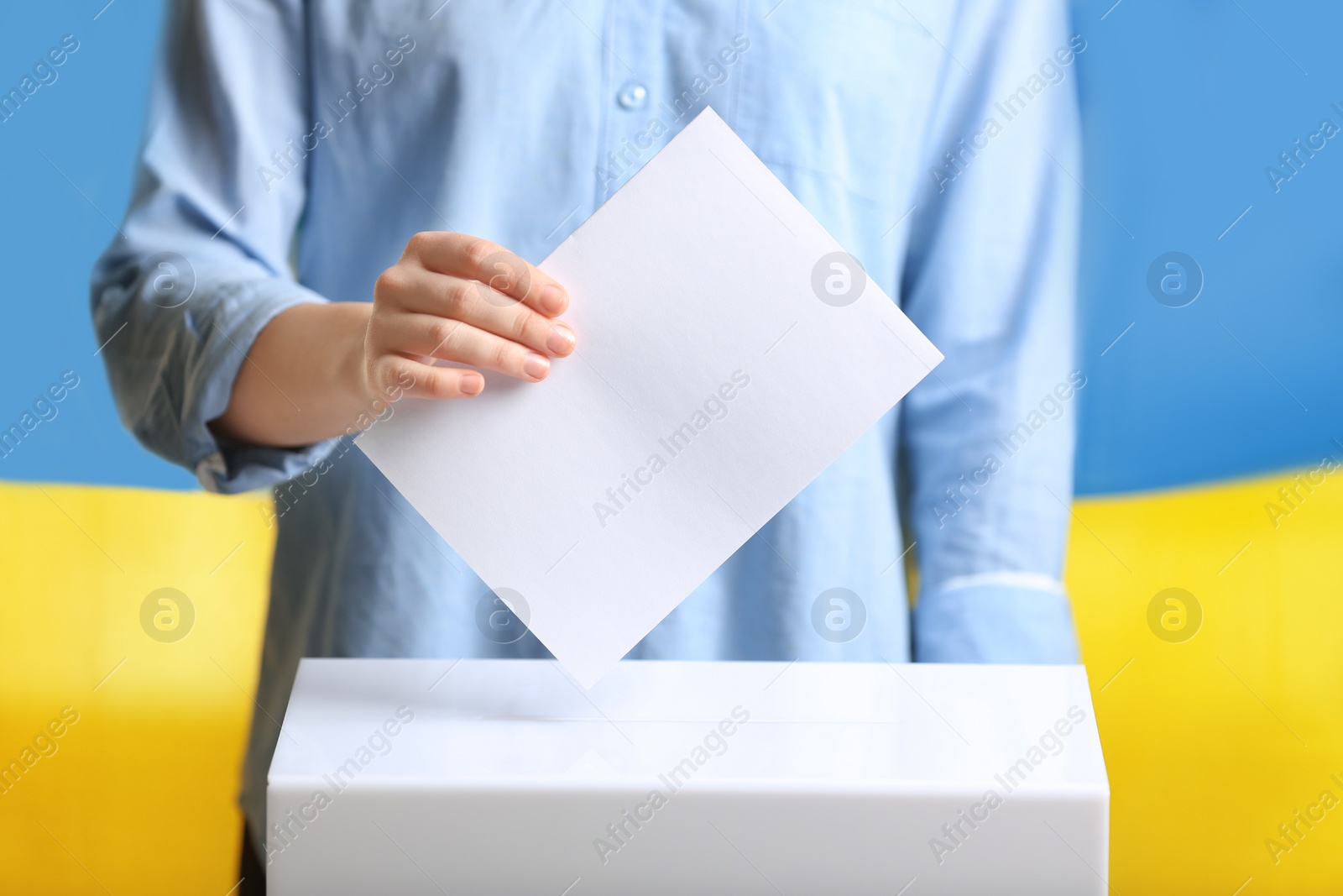 Photo of Woman putting voting paper into ballot box against Ukrainian flag, closeup