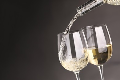 Photo of Pouring white wine into glass against grey background, closeup. Space for text