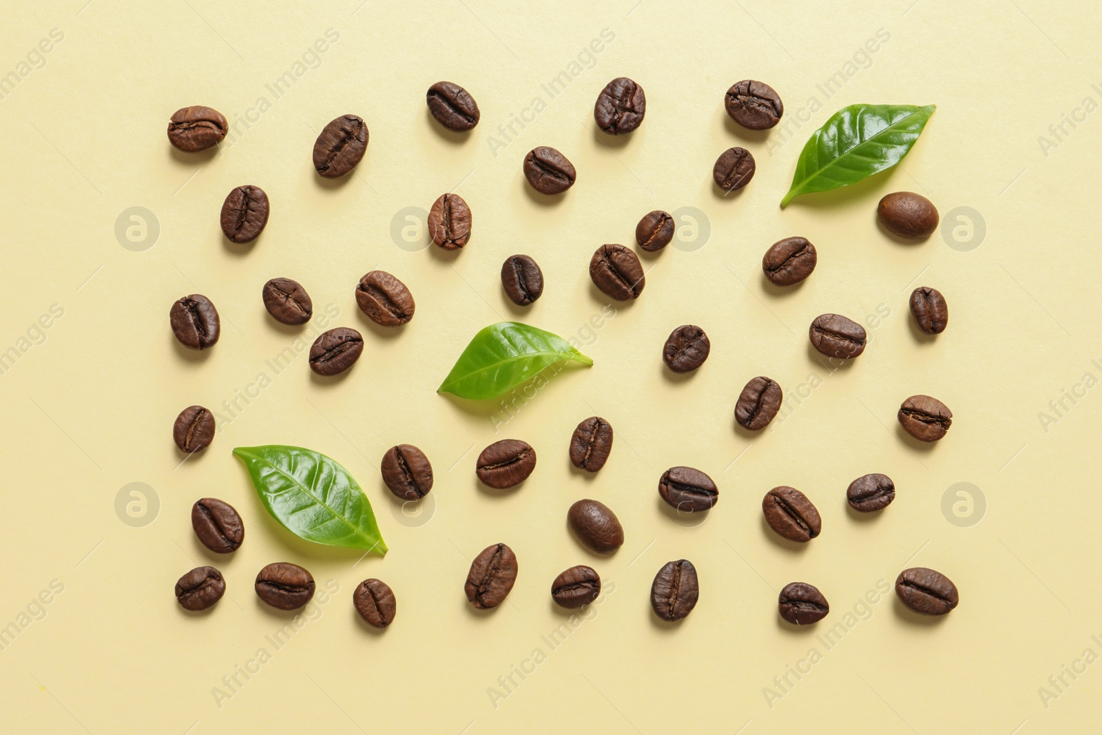 Photo of Fresh green coffee leaves and beans on light yellow background, flat lay