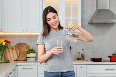 Photo of Woman pouring water from jug into glass in kitchen