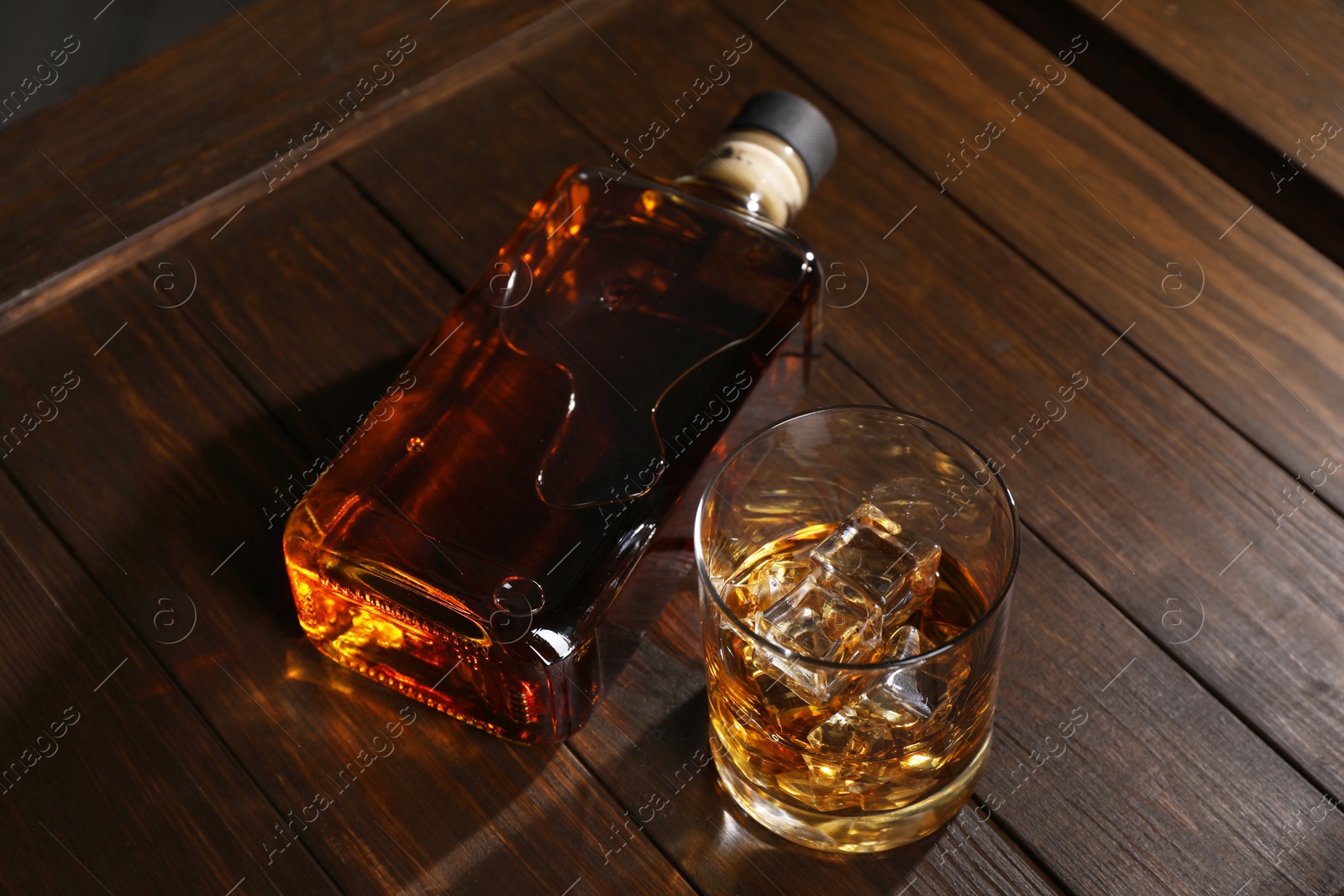 Photo of Whiskey with ice cubes in glass and bottle on wooden crate