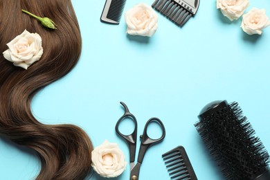 Photo of Flat lay composition with professional hairdresser tools, flowers and brown hair strand on light blue background. Space for text