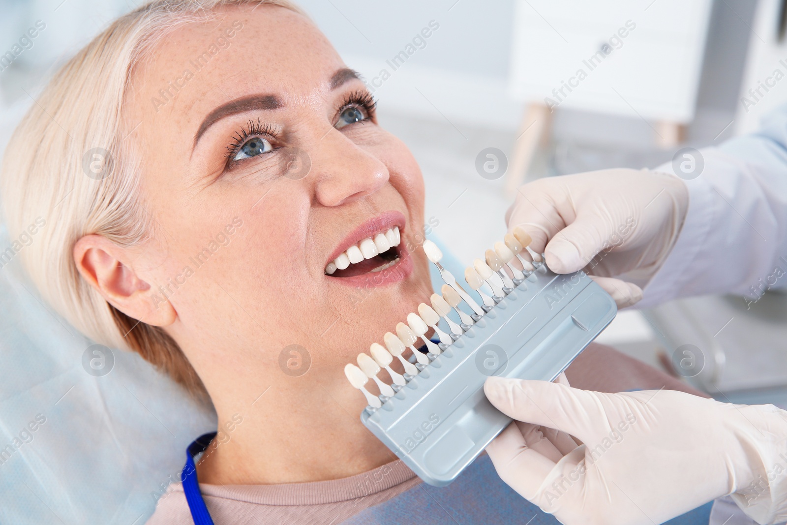 Photo of Dentist selecting patient's teeth color with palette in clinic
