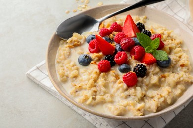 Photo of Bowl of oatmeal porridge served with berries on light grey table, closeup