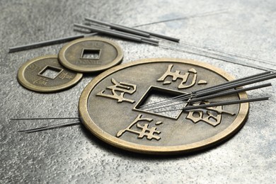 Photo of Acupuncture needles and Chinese coins on grey textured table, closeup