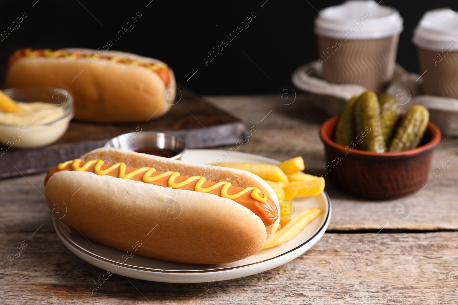 Photo of Delicious hot dog with mustard and French fries on wooden table, closeup