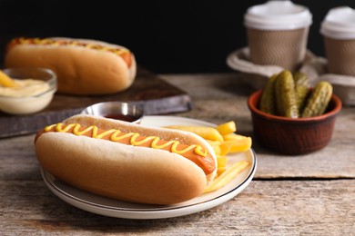 Delicious hot dog with mustard and French fries on wooden table, closeup