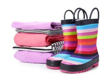 Photo of Colorful children's rubber boots and stack of clothes on white background