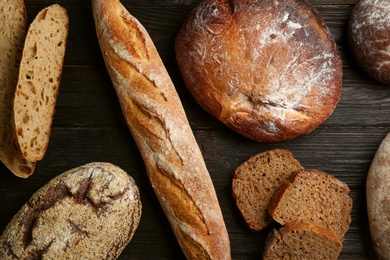 Photo of Different kinds of fresh bread on black wooden table, flat lay
