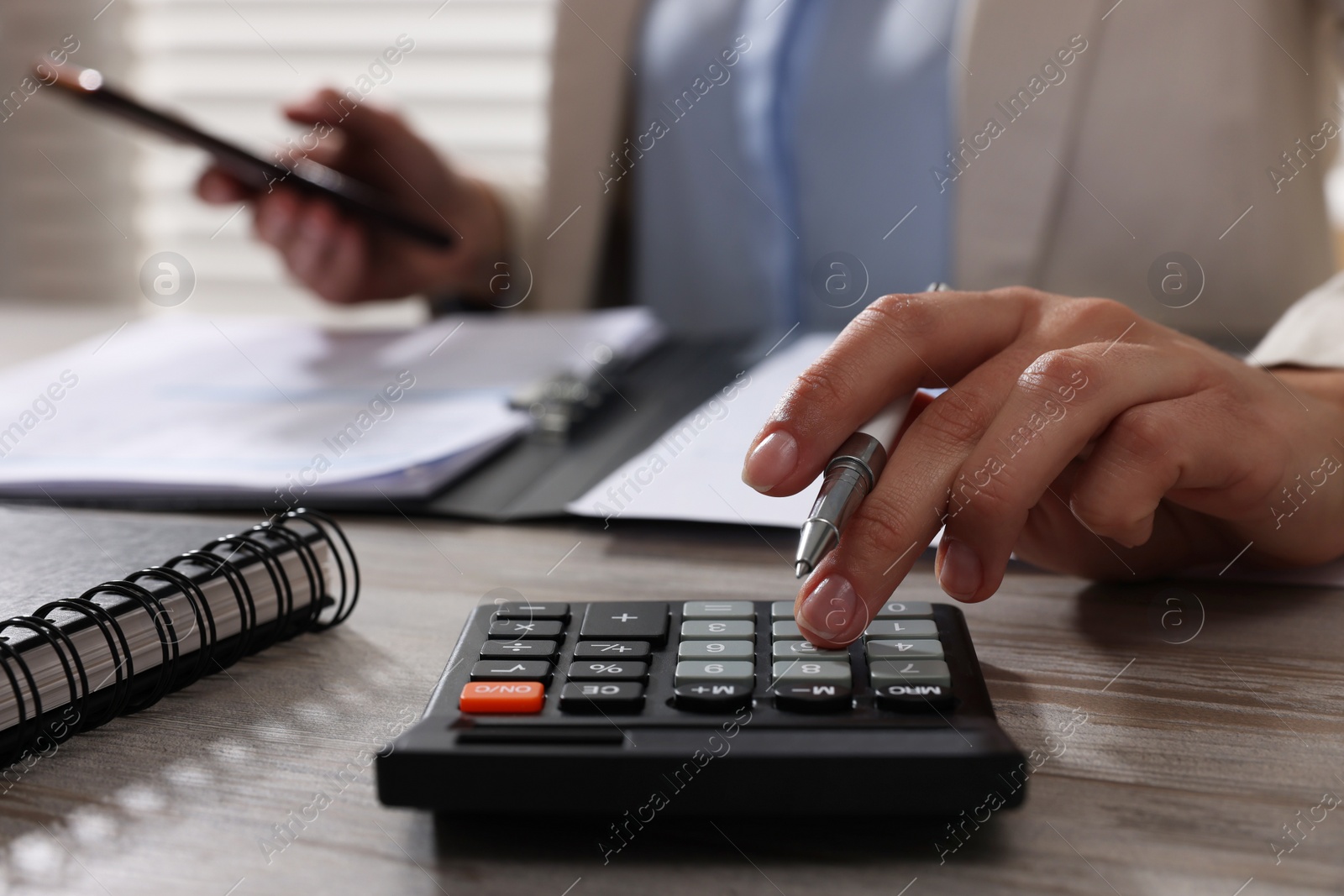 Photo of Woman using calculator at light wooden table in office, closeup