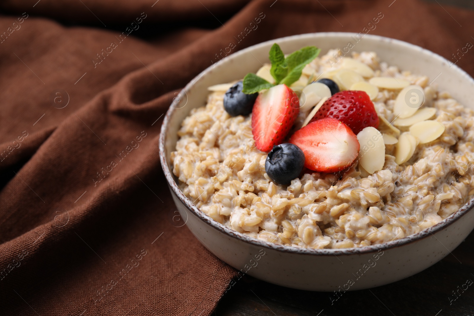 Photo of Tasty oatmeal with strawberries, blueberries and almond flakes in bowl on wooden table, closeup. Space for text