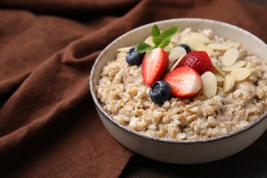 Photo of Tasty oatmeal with strawberries, blueberries and almond flakes in bowl on wooden table, closeup. Space for text