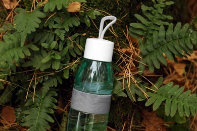 Photo of Glass bottle of fresh water on ground in forest, above view
