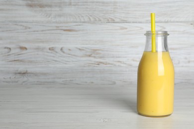 Photo of Bottle of tasty smoothie with straw on white wooden table. Space for text