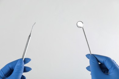 Photo of Dentist holding mouth mirror and plugger on light background, closeup