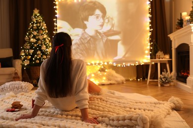 MYKOLAIV, UKRAINE - DECEMBER 24, 2020: Woman watching Harry Potter and Philosopher's Stone movie via video projector in room. Cozy winter holidays atmosphere
