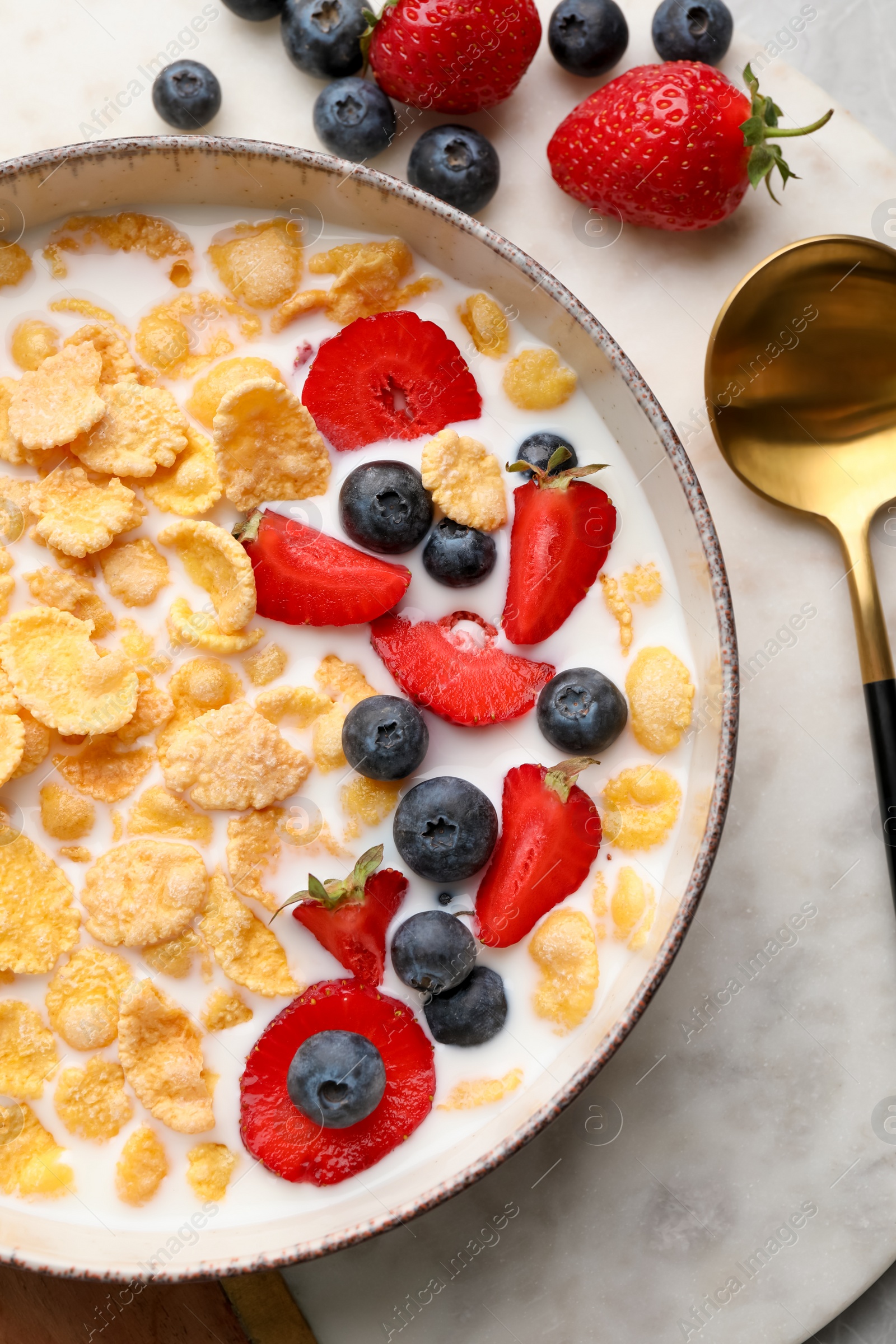 Photo of Bowl of tasty crispy corn flakes with milk and berries on table, flat lay