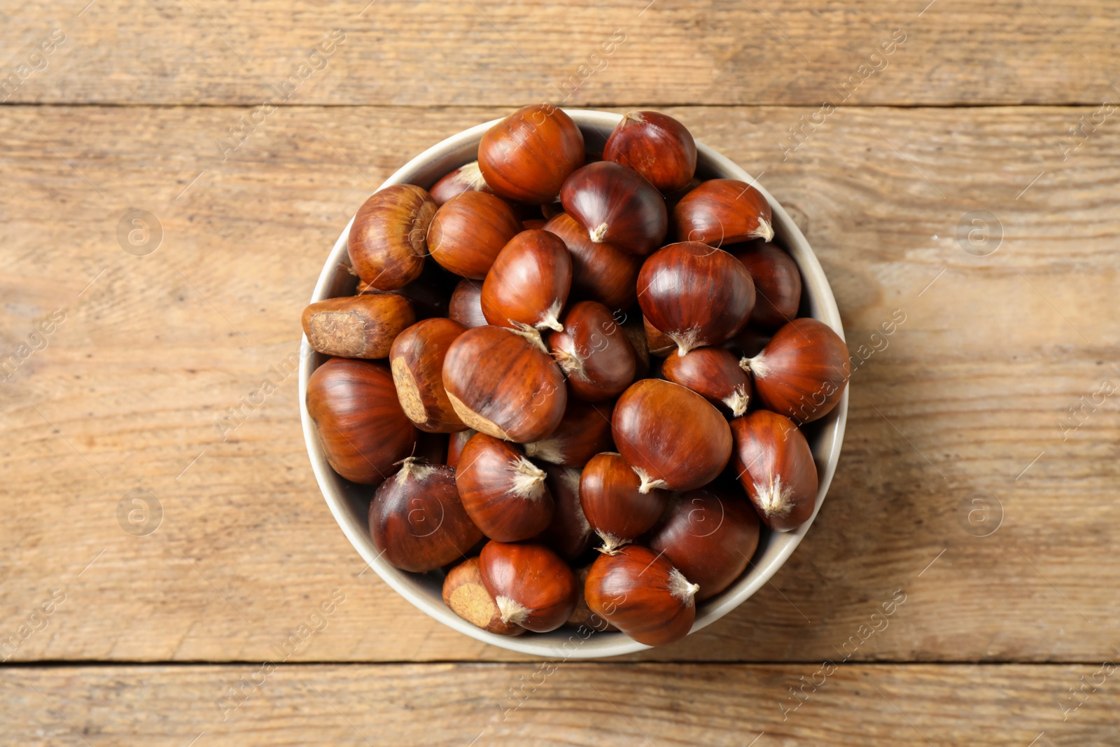 Photo of Fresh sweet edible chestnuts in bowl on wooden table, top view