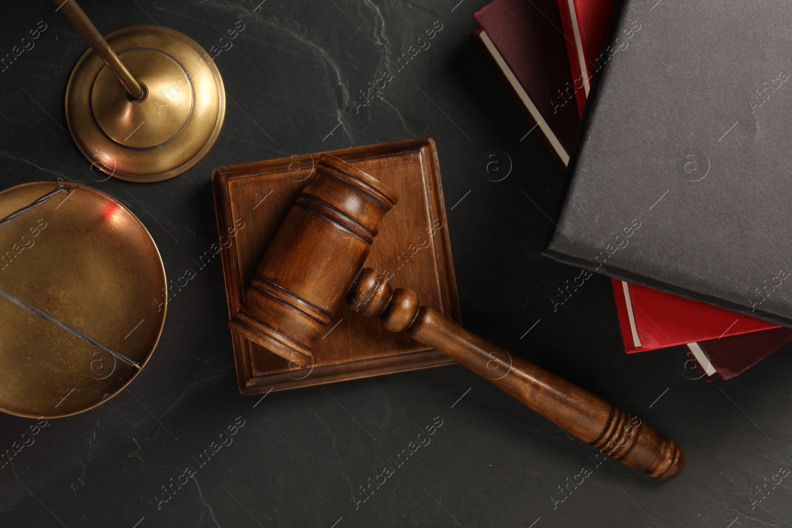 Photo of Wooden gavel, sound block and books on dark textured table, flat lay