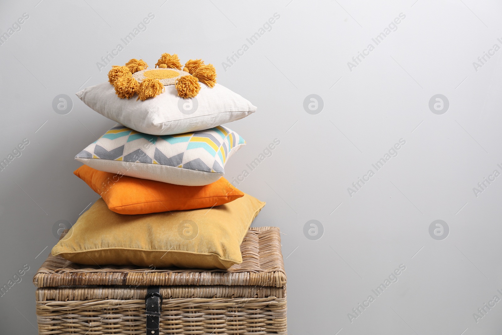 Photo of Soft pillows on wooden trunk near light grey wall, space for text