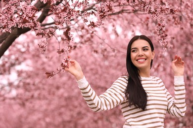 Pretty young woman in park with blooming trees. Spring look