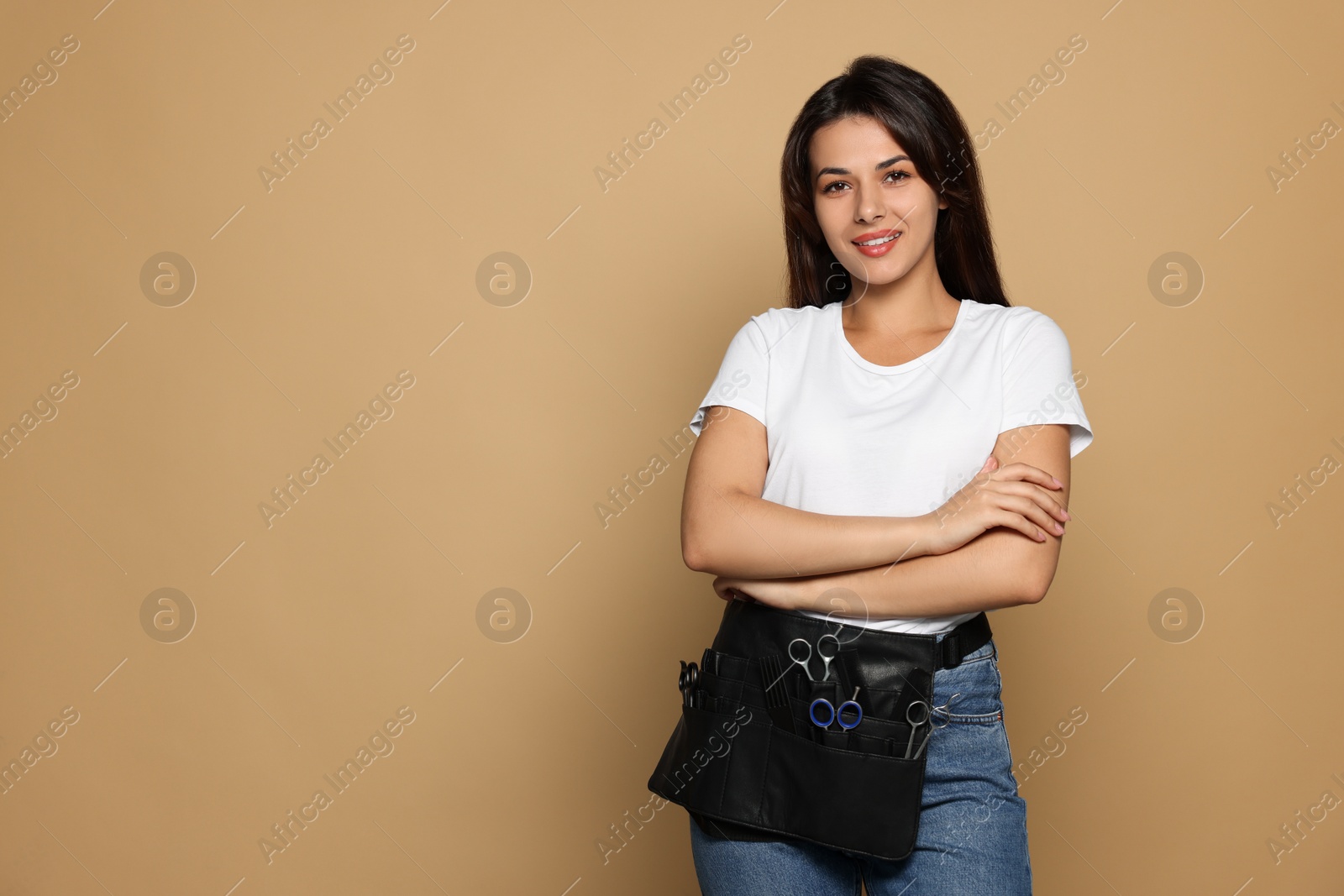 Photo of Portrait of happy hairdresser with professional tools on pale orange background. Space for text