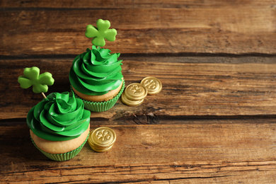 Photo of Delicious decorated cupcakes and coins on wooden table, space for text. St. Patrick's Day celebration