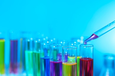 Dripping liquid from pipette into test tube on light blue background, closeup