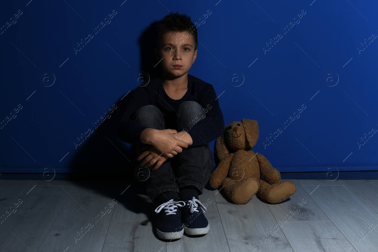 Photo of Abused little boy with toy near blue wall. Domestic violence concept