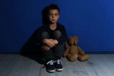 Abused little boy with toy near blue wall. Domestic violence concept