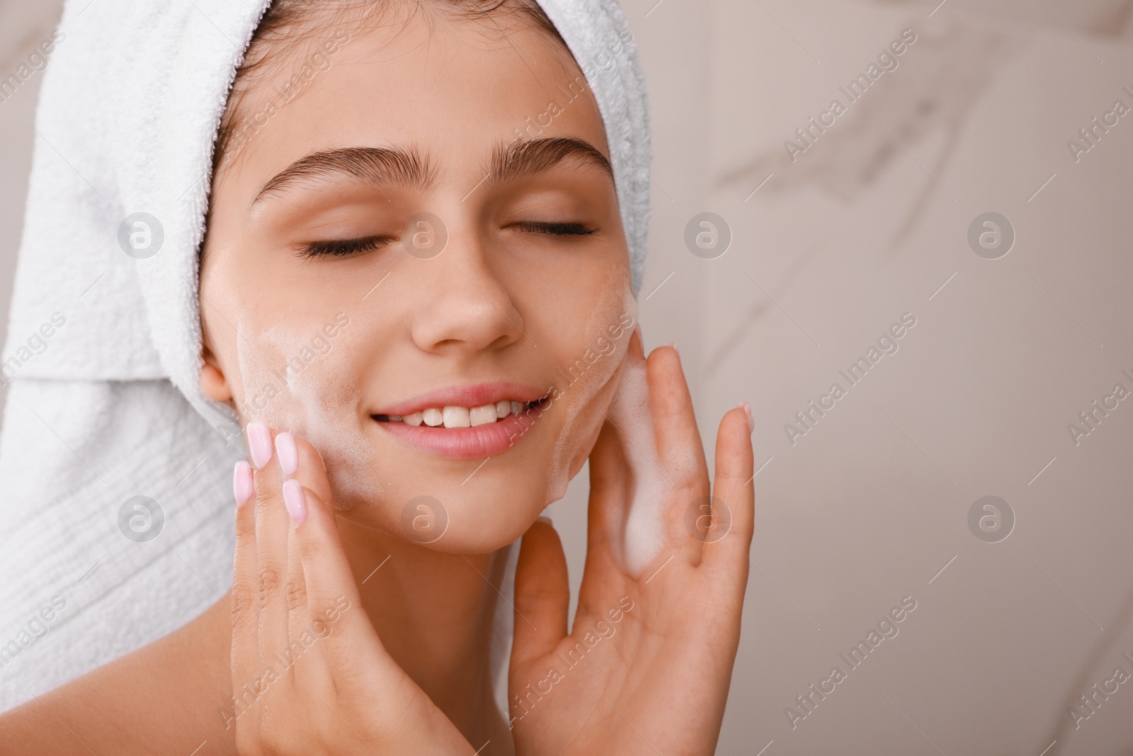 Photo of Beautiful teenage girl applying cleansing foam onto face in bathroom, closeup. Skin care cosmetic