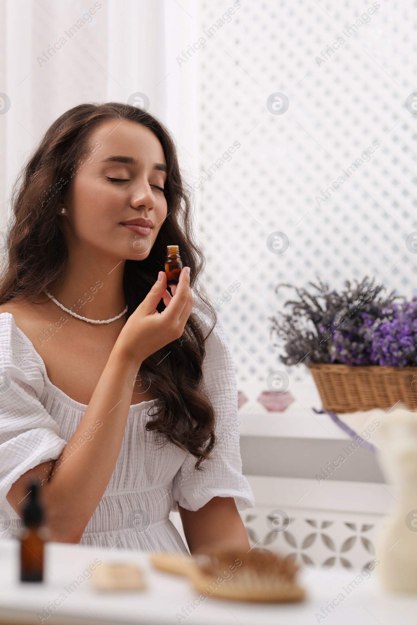 Photo of Beautiful young woman with bottle of essential oil at table indoors