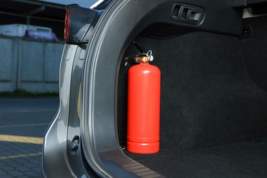 Photo of Red fire extinguisher in trunk, space for text. Car safety equipment