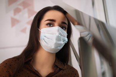 Sad young woman in protective mask indoors. Self-isolation during coronavirus pandemic