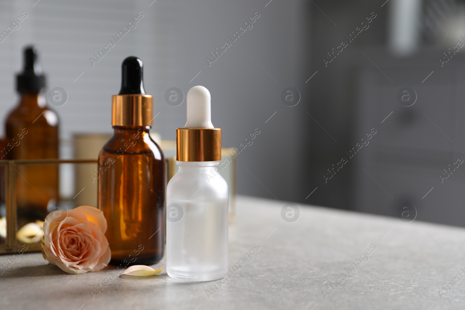 Photo of Bottles of cosmetic serum and flower on gray table, closeup. Space for text