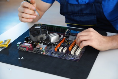 Photo of Male technician repairing motherboard at table, closeup
